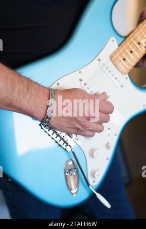 Primo piano di un musicista rock che suona una chitarra elettrica blu e indossa un bracciale con polsino d'argento Foto Stock