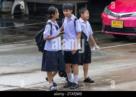 SAMUT PRAKAN, THAILANDIA, 20 settembre 2023, allegri scolari in uniforme camminano lungo una strada piovosa Foto Stock