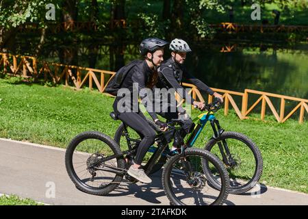 Una coppia beata, adornata con attrezzatura da ciclismo professionale, si gode una romantica passeggiata in bicicletta attraverso un parco circondato da moderne attrazioni naturali Foto Stock