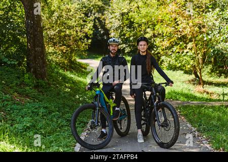 Una coppia beata, adornata con attrezzatura da ciclismo professionale, si gode una romantica passeggiata in bicicletta attraverso un parco circondato da moderne attrazioni naturali Foto Stock