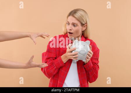 Truffatore che prende salvadanaio da una donna spaventata su sfondo beige. Attenzione - frode Foto Stock