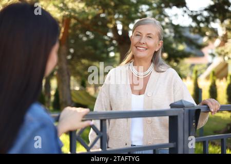 Rapporto amichevole con i vicini. Donne felici vicino alla recinzione all'aperto Foto Stock