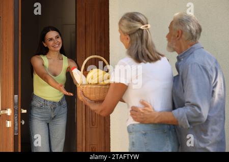 Rapporto amichevole con i vicini. Coppia anziana con cesto di vimini di prodotti che trattano giovani donne all'aperto Foto Stock