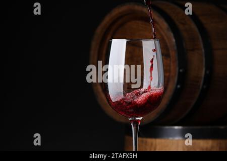 Versare il vino rosso nel bicchiere vicino a botti di legno su sfondo nero. Spazio per il testo Foto Stock