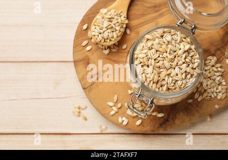 Orzo perlato secco in vaso di vetro e cucchiaio su un tavolo in legno chiaro, vista dall'alto. Spazio per il testo Foto Stock