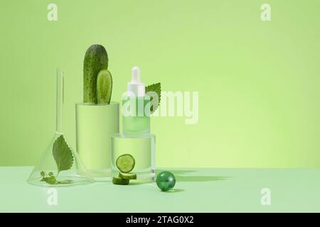 Tema salute e bellezza. Cosmetici naturali con estratti di cetriolo e foglie di perla. Flacone per siero trasparente e puntali in vetro su ba verde pastello Foto Stock