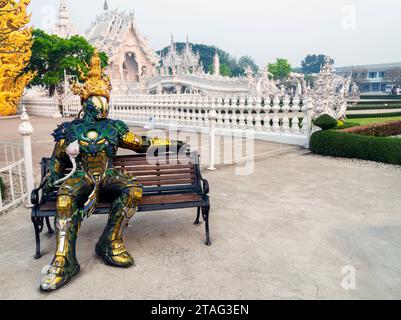Chiang Rai, Thailandia - marzo 29 2023: Seduto su una panchina accanto ai cancelli d'ingresso del famoso tempio e delle principali opere d'arte, progettato dal maestro artista Chale Foto Stock