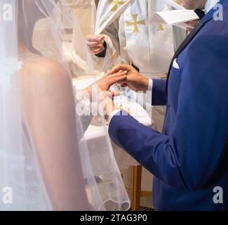 Sposo che mette un anello al dito della sposa in una cerimonia nuziale Foto Stock