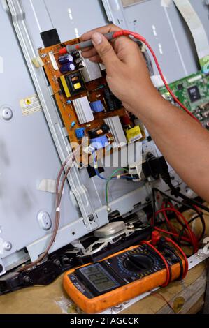 Cairo, Egitto, 3 ottobre 2023: Ingegnere tecnico che utilizza un multimetro digitale, circuito di alimentazione della scheda principale TV LCD, fili, trasformatori, resis Foto Stock