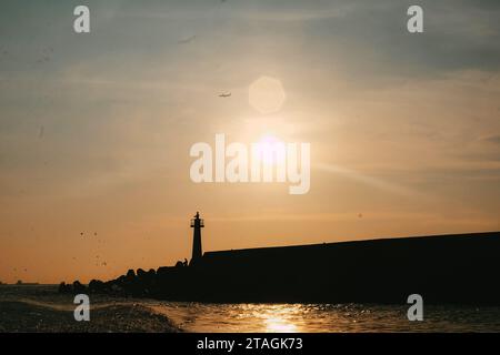 Tramonto sul faro più alto. Vista angolare ridotta della silhouette dell'aereo che vola contro il cielo durante il tramonto con luce parassita. Foto Stock