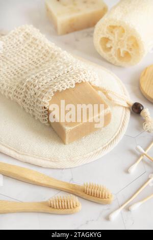 Sapone beige organico fatto a mano in un sacchetto salvasapone vicino a articoli igienici - spugne naturali, spazzolini da denti di bambù e tamponi di cotone da vicino. Erbe naturali Foto Stock