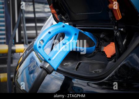 Ricarica per auto elettriche nel parcheggio con stazione di ricarica per auto elettriche sulla strada della città. Primo piano dell'alimentatore collegato di colore blu a una c Foto Stock