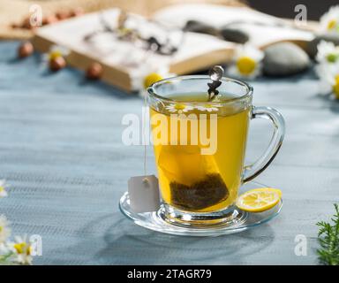 Sacchetto di tè alle erbe in una tazza di vetro. Sacchetto di tè in camomilla. Bevande calde alla scrivania Foto Stock