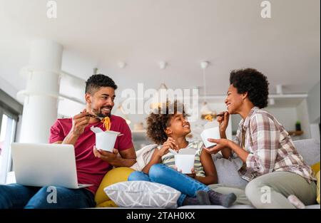 Felice famiglia africana che mangia in salotto e si diverte a trascorrere del tempo insieme. Piatti da asporto casalinghi Foto Stock