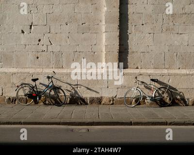 Due biciclette di fronte l'una all'altra contro il muro di pietra di una chiesa italiana al sole d'estate Foto Stock