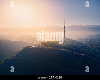 Foto aerea con drone della torre della televisione simbolo di Almaty e parcheggia sulla collina di Koktobe contro le montagne di neve all'alba in Kazakistan Foto Stock