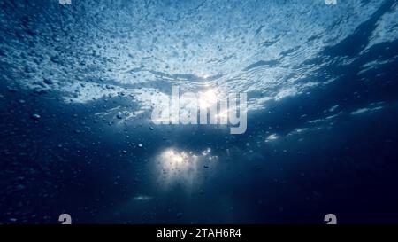 Vista da sotto il fondo del mare sui raggi del sole che brillano attraverso la superficie dell'acqua. Bolle d'aria in aumento scintillanti e scintillanti alla luce. Foto Stock