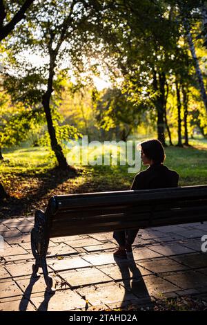 Giovane donna elegante con i capelli corti in occhiali siede in un parco Foto Stock