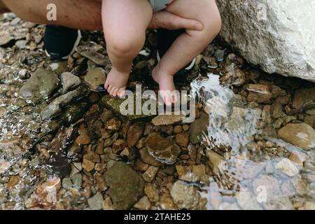 Papà che tiene i piedi del bambino in un torrente Foto Stock