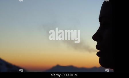 la silhouette di una giovane donna respira vapore durante un freddo tramonto Foto Stock