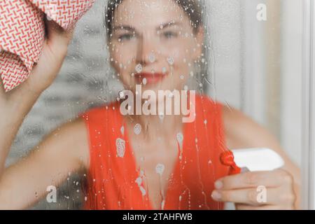 Donna che fa pulizia, lavando la porta di vetro con detergente e straccio Foto Stock