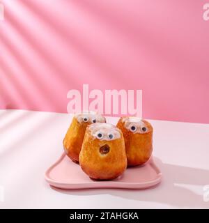 tre cupcake con occhi incollati su un piatto rosa Foto Stock