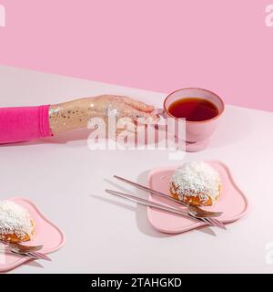 la mano di una donna tiene una tazza di tè rosa accanto a un piatto con un panino Foto Stock