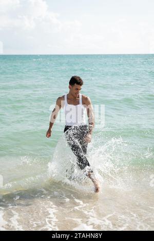 Un giovane cubano sorridente e muscoloso che si diverte mentre si trova in acqua oceanica a Miami South Beach Foto Stock