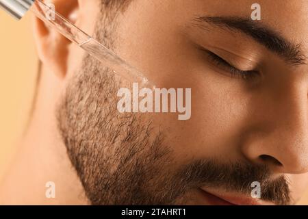 Uomo che applica siero cosmetico sul viso, primo piano Foto Stock