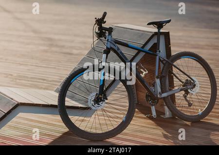 Mountain bike parcheggiata sul molo di legno al tramonto, con una lunga ombra Foto Stock