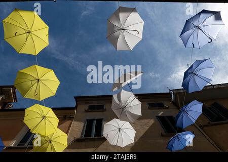 Gli ombrelli colorati blu, bianco e giallo sono appesi come decorazione sopra le strette stradine di un pittoresco villaggio in Toscana, Italia Foto Stock