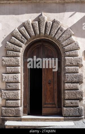 Porta in legno e arco in pietra segnano l'ingresso di un edificio a Montepulciano, un villaggio di montagna in Toscana, Italia. Foto Stock