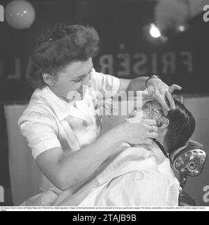 Radersi negli anni '1940 Una giovane donna sta radendo un uomo al barbiere. Utilizza un rasoio dritto e viene mostrato qui mentre si esegue la rasatura, chiudere l'orecchio dell'uomo. 1945. Foto Kristoffersson rif. N98-6 Foto Stock