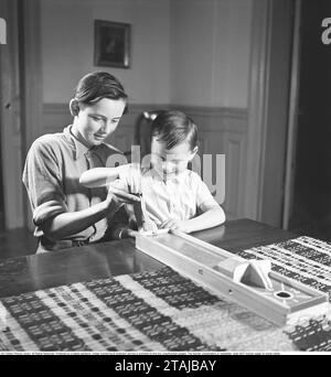 I bambini giocano negli anni '1940 In assenza della televisione e di Internet, i bambini degli anni '1940 passarono il loro tempo libero, tra le altre cose. con i giochi da tavolo. Qui, due ragazzi che giocano a un gioco in cui lo scopo è quello di ottenere una moneta lungo una pista di legno. Viene fatto cadere e rotola lungo una pista e l'obiettivo è quello di far fermare la moneta su una parte della pista che dà il punteggio più alto. 1949. Kristoffersson rif. AU62-5 Foto Stock