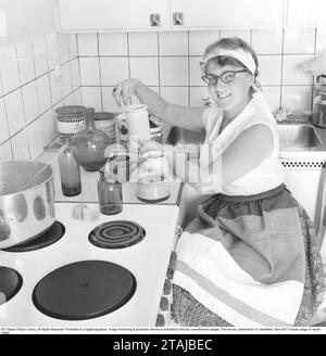 In cucina anni '1950 Interno di una cucina e di una giovane donna con diversi tipi di contenitori, brocche, bottiglie di vetro e vasetti. 1959 Foto Stock