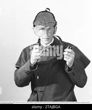 Fare il detective. Un uomo vestito con i vestiti tipici mentre il famoso detective fittizio Sherlock Holmes guarda la macchina fotografica attraverso una lente di ingrandimento. Foto Stock