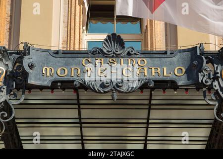 Cartello sopra l'ingresso principale esterno di Monte Carlo / Monte-Carlo Casino, Monaco. Una bandiera vola nella brezza estiva. (135) Foto Stock