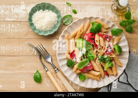 Penne per pasta integrale con broccoli e peperoni rossi grigliati e su un tavolo rustico in legno chiaro. Pasta vegana. Cucina tradizionale italiana Foto Stock