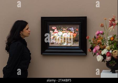 LONDRA, REGNO UNITO - 01 DICEMBRE 2023: Un membro dello staff della galleria guarda un dipinto di Clara Peeters intitolato "natura morta di rose, garofani, tulipani, narcisi, Iris, Love-in-a-Mist, larkspur e altri fiori, in un cestino di vimini, con una farfalla e un cricket' (stima: £ 500.000-700.000) durante una foto alla casa d'aste Sotheby's che mostra i punti salienti delle vendite della Old Masters Week a Londra, Regno Unito il 1° dicembre 2023. Gli sconti serali della settimana dei maestri di dicembre si estendono tra l'inizio del XV e l'inizio del XX secolo e includono una vasta gamma di opere notevoli provenienti da vicino Foto Stock