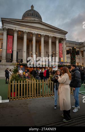 Londra, Regno Unito - 20 novembre 2023: Mercato di Natale di Trafalgar Square, Londra con persone in un bar all'aperto. La National Gallery di Trafalgar Square è dietro. Foto Stock