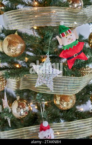 Decorazioni natalizie, palline luccicanti dorate, una stella luccicante e un elfo appesi su un albero di natale. Verticale Foto Stock