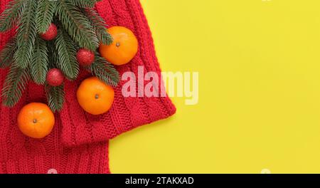 Sciarpa a maglia rossa, mandarini e ramoscello di abete rosso su sfondo giallo, vista dall'alto, spazio copia. Composizione natalizia, anno nuovo, banner. Bran di Capodanno Foto Stock