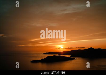 Tramonto arancione su sagome di montagne in riva al mare Foto Stock