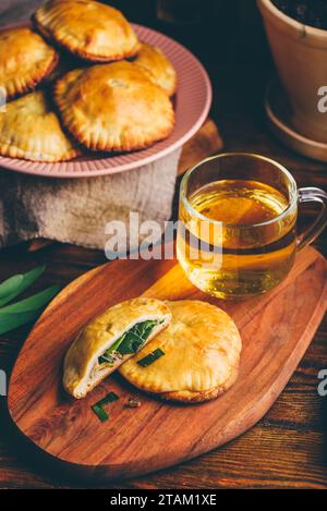 Dolci al forno ripieni di erba cipollina siberiana e funghi con tazza di tè verde su vassoio di legno Foto Stock