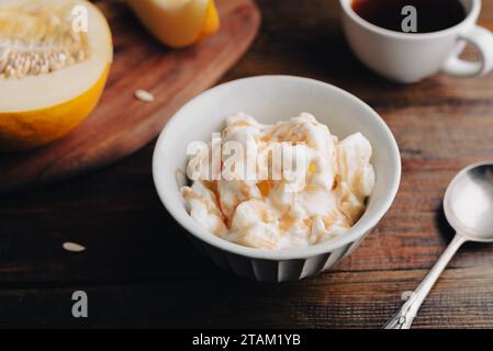 Gelato al melone fatto in casa con sciroppo di frutta in ciotola d'epoca e tazza di caffè su tavolo rustico Foto Stock