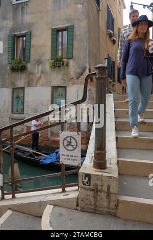 Segni di sovra-turismo che sorpassa Venezia e buone maniere: Non sederti, un cartello sulle scale del ponte, piccoli spazi dove i turisti possono riposare Foto Stock