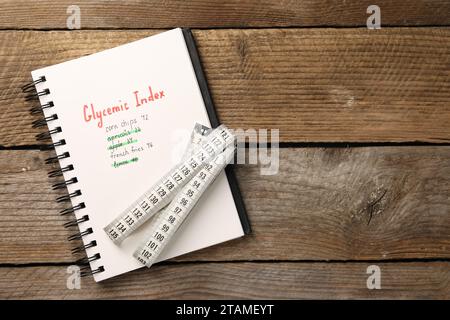 Indice glicemico. Notebook con informazioni e metro a nastro su tavolo in legno, vista dall'alto. Spazio per il testo Foto Stock