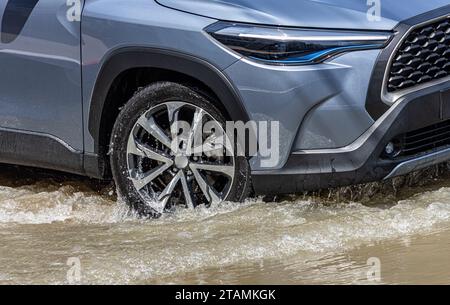 Un'auto attraversa una strada allagata della città Foto Stock