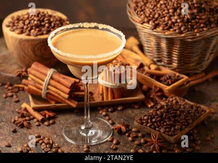 Cocktail martini al cioccolato o liquore irlandese con crema su sfondo marrone. I chicchi di caffè, i bastoncini di cannella e l'anice sono sparsi sul tavolo. Foto Stock