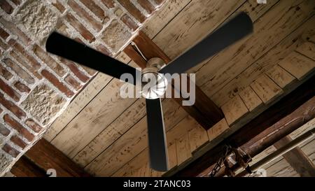 Ventilatore d'aria a soffitto che gira lentamente su vecchi soffitti in legno e mattoni antichi. Foto Stock